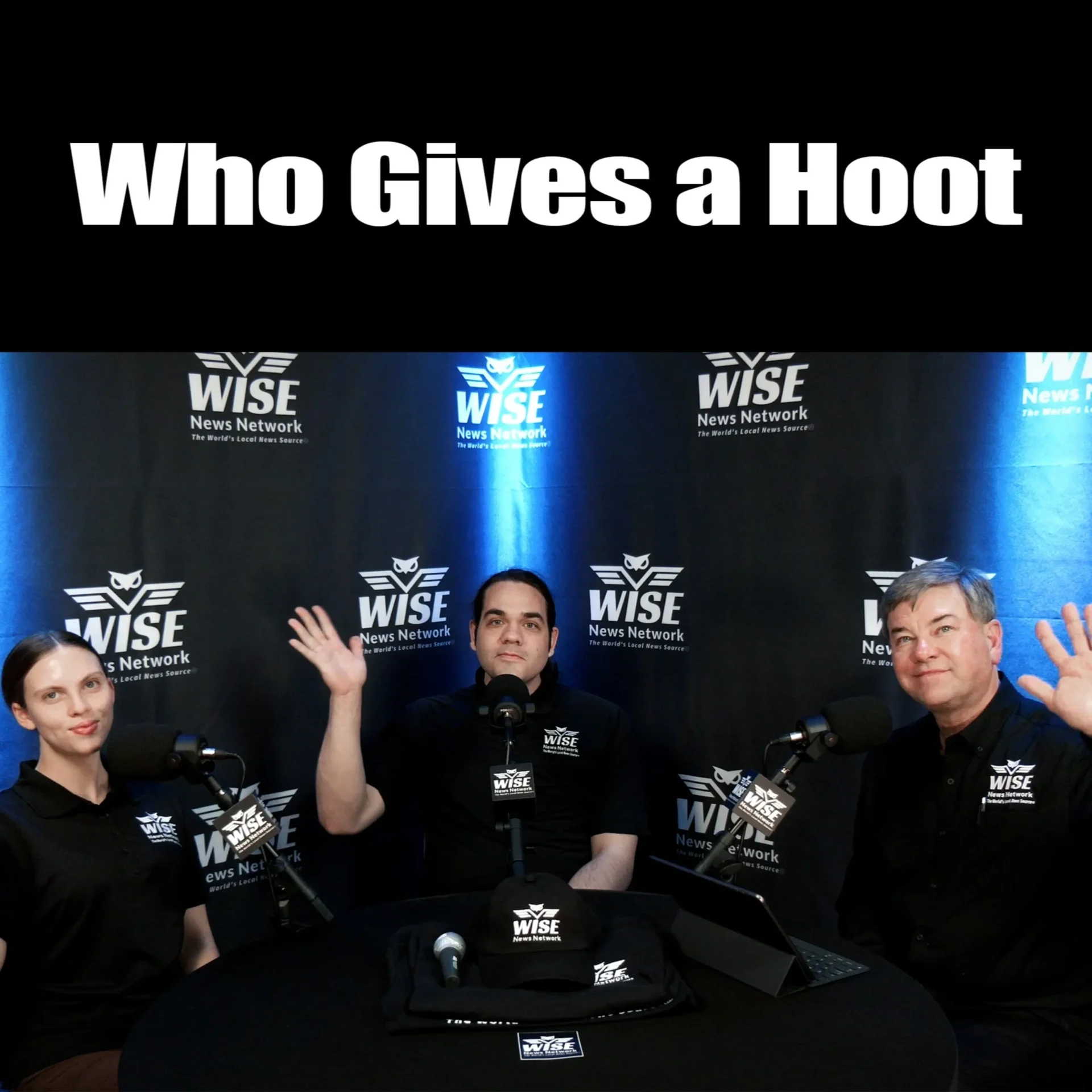 Three people in black shirts, seated at a table with microphones, wave towards the camera. The backdrop displays "Wise News Network" logos, and large text above them reads "Who Gives a Hoot".