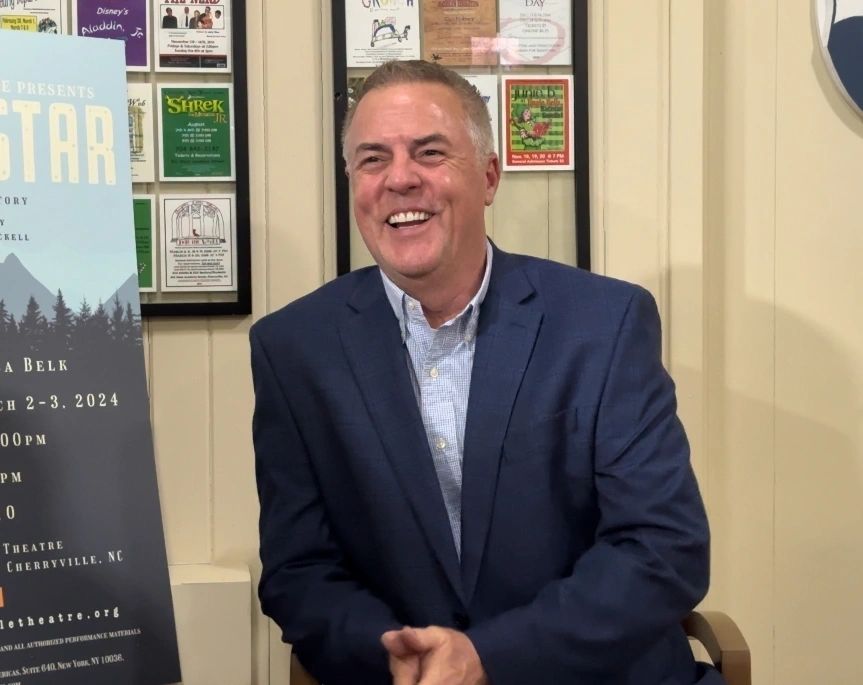 A man in a suit sitting next to a sign.