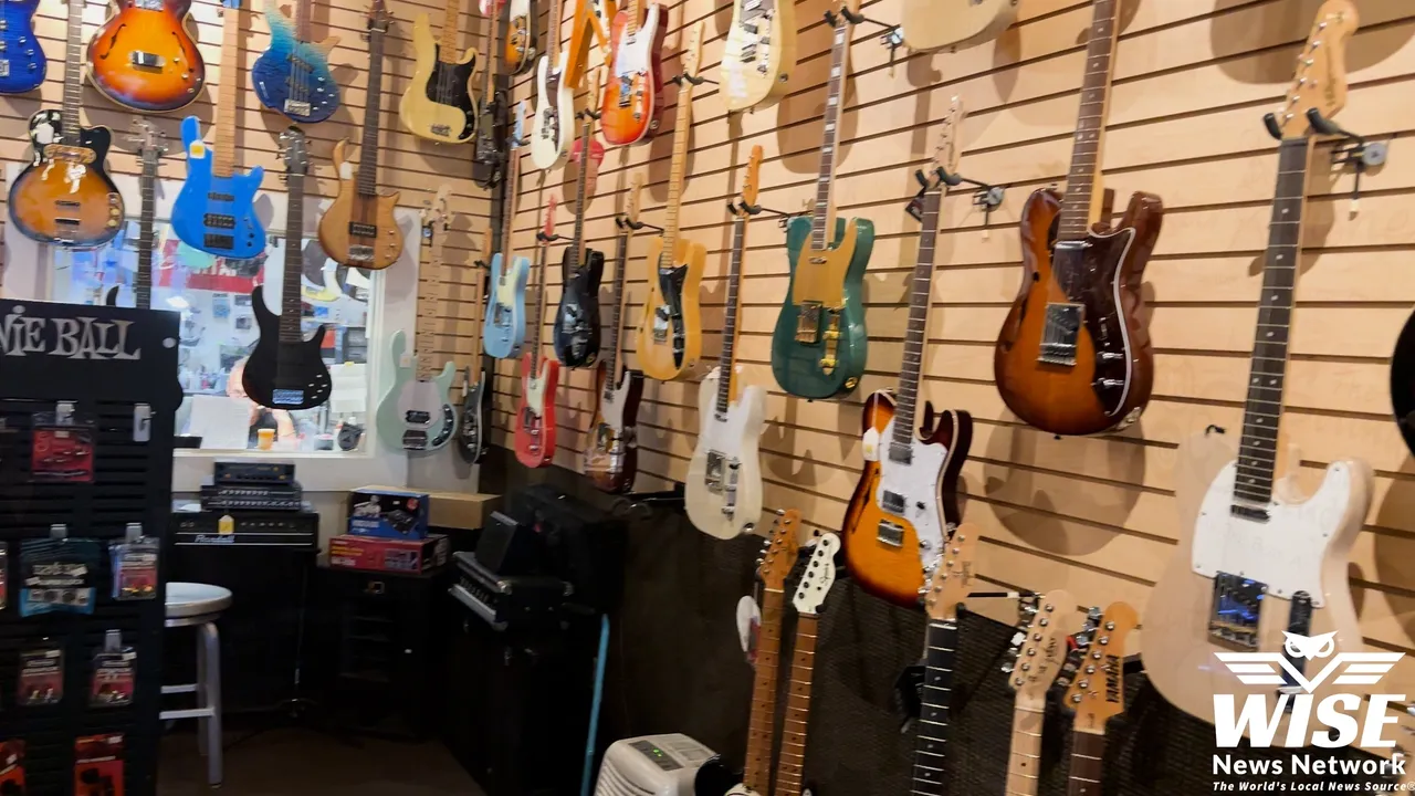 A shop with various guitars displayed on wall mounts, ranging in colors and styles. There are amplifiers and other musical equipment on the floor. A sign with "WISE News Network" is visible in the bottom right corner.