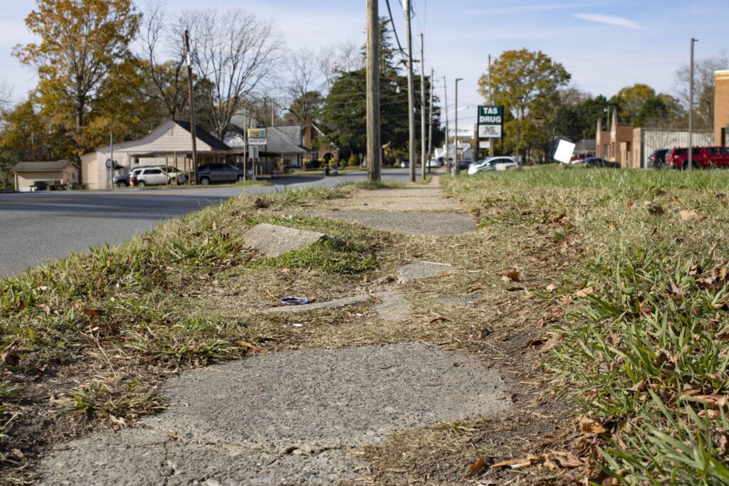 A broken sidewalk with large displaced chunks of concrete and grass growing in. 