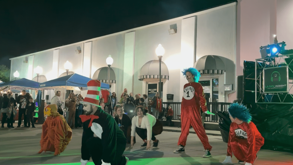 A group of dancers dressed up as Dr. Seuss characters with a crowd watching from the side. 