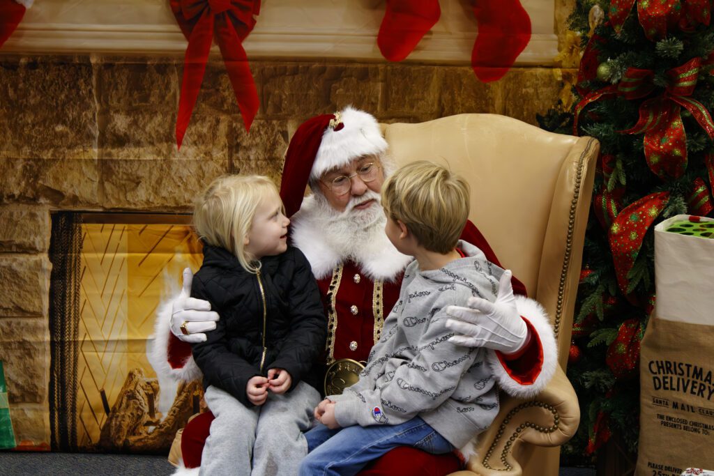 A man dressed as Santa Claus holding two young children. 