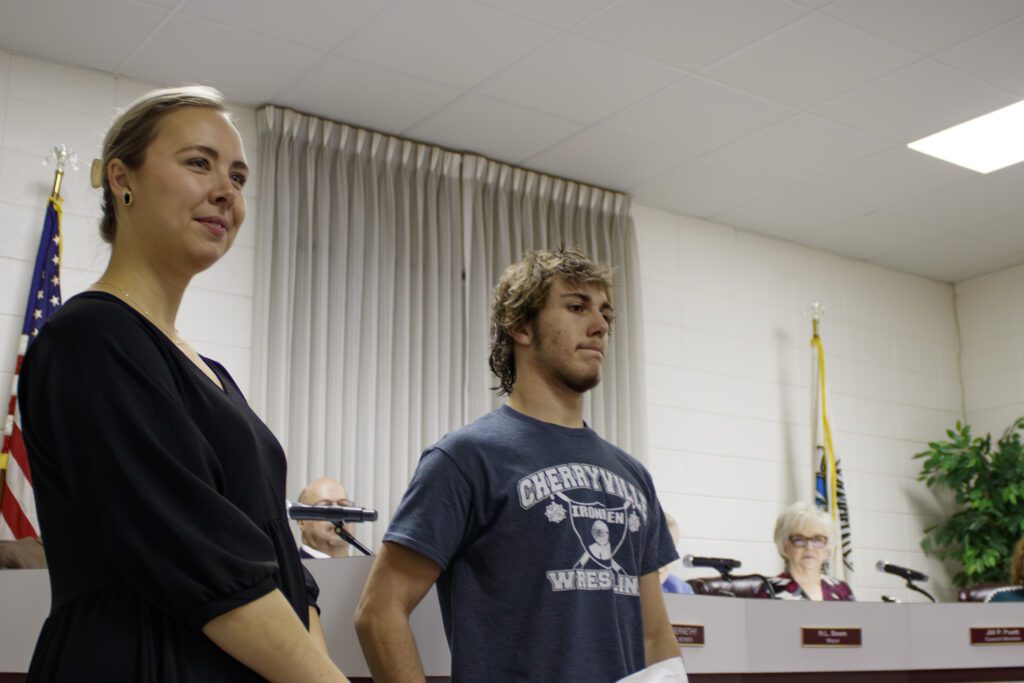 A man and woman, the woman wearing a black dress and the man wearing black jeans and a blue shirt with the cherryville wrestling team logo.