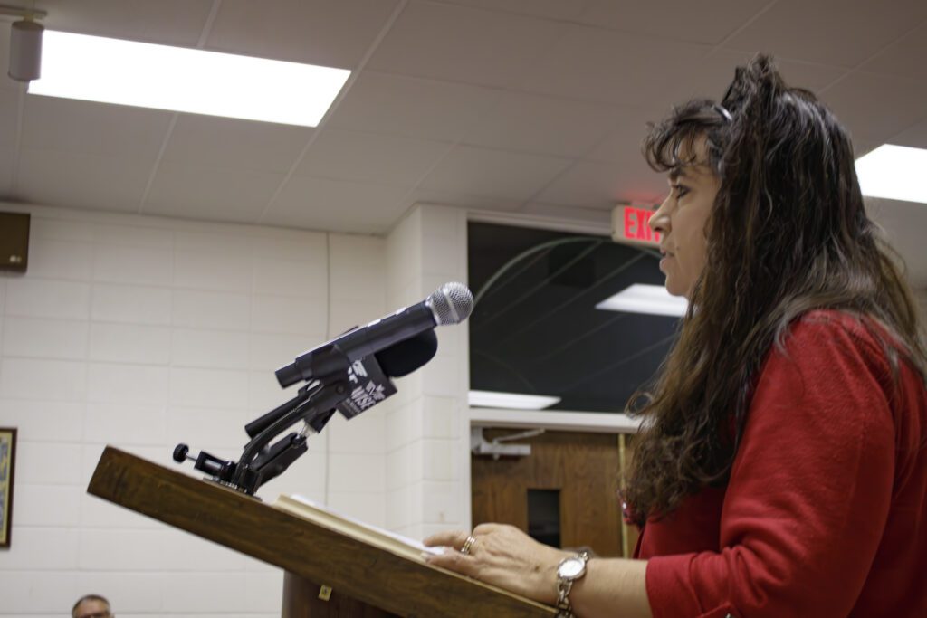 A woman speaking at a podium wearing a red shirt. 