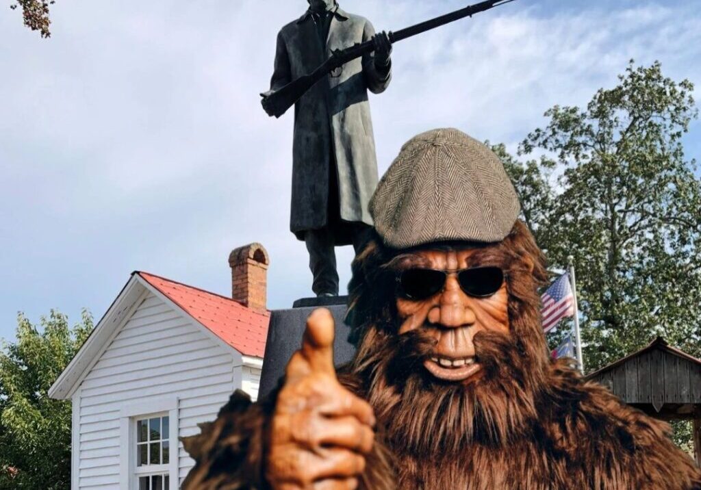 A man in a bear costume with a rifle and a statue of a person.