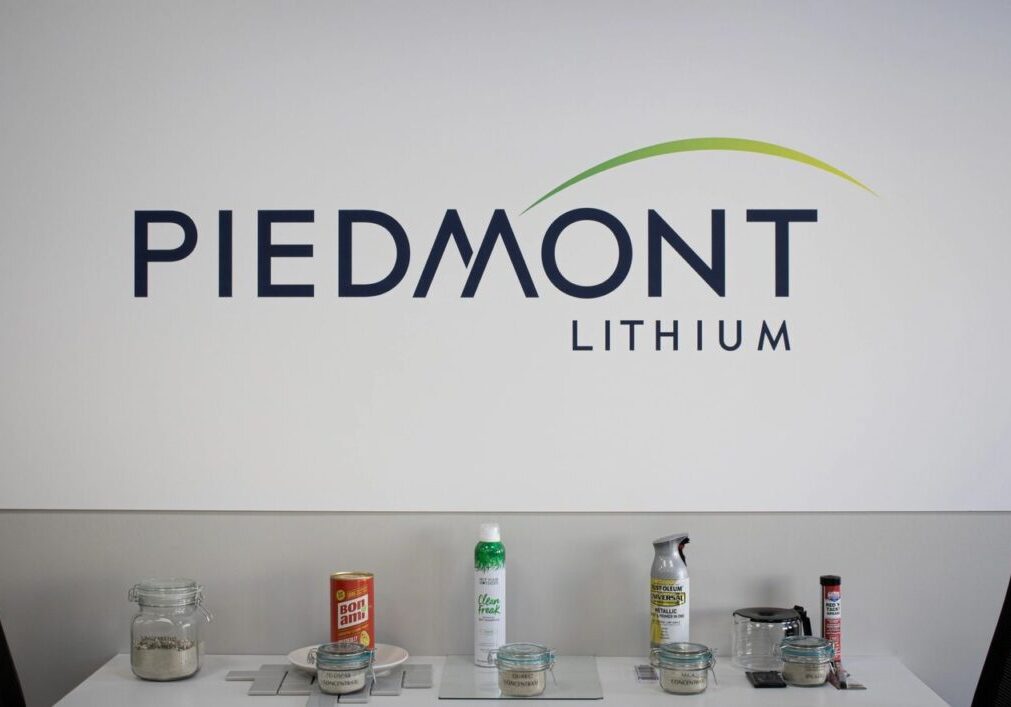 A table with various jars and containers in front of a wall displaying the Piedmont Lithium company logo.