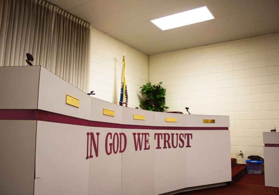 A church with a large white wall and a sign that says " in god we trust ".