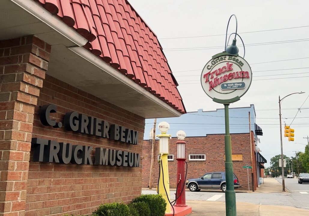 Brick building with a sign for G. Grier Beam Truck Museum, located on a street corner with vintage gas pumps and a sign featuring the museum's name.