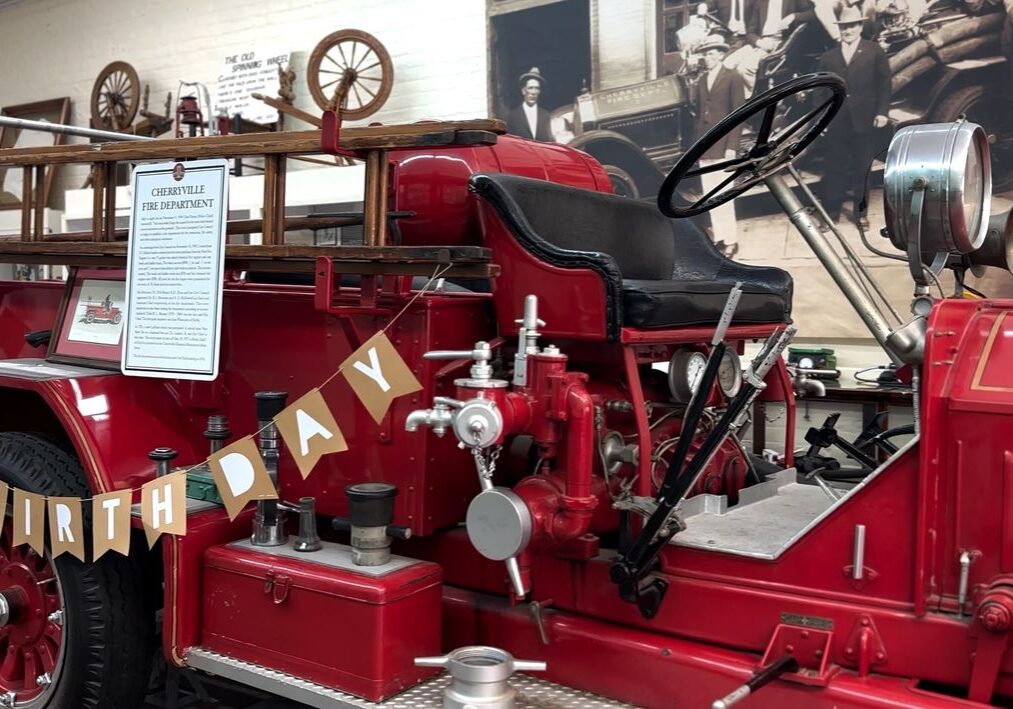 A vintage red fire truck displayed in a museum setting, decorated with a "Happy Birthday" banner.